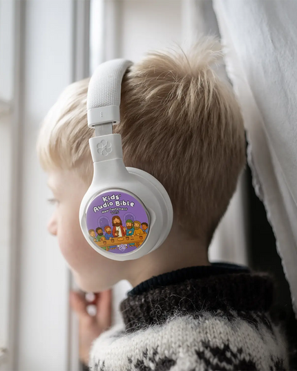 Boy wearing white ONANOFF StoryPhones  kids headphones listening to StoryShields Kids’ Audio Bible – New Testament Volume 5”. The child is gazing out of a window, listening to engaging audio stories. The scene highlights child-friendly wireless headphones ideal for storytelling and educational listening experiences.